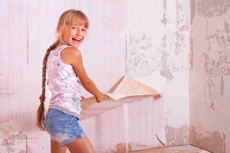 Chica se divierte quitando papel pintado de la pared