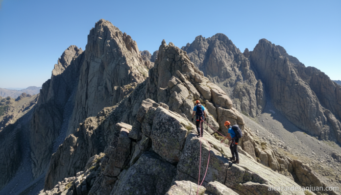 Mountain ridge hike in Sierra de Gredos, Spain, granite peaks under clear blue sky, two mountaineers with safety harness p...
