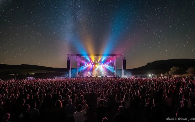 Outdoor music festival at night in La Mancha region, Spain. Large crowd watching a rock concert on a big stage with colorf...
