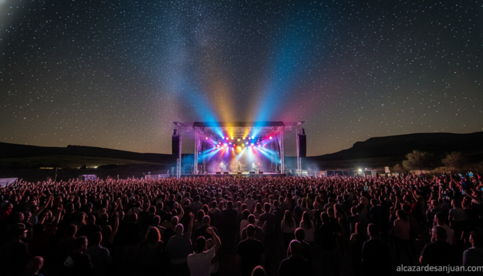 Outdoor music festival at night in La Mancha region, Spain. Large crowd watching a rock concert on a big stage with colorf...