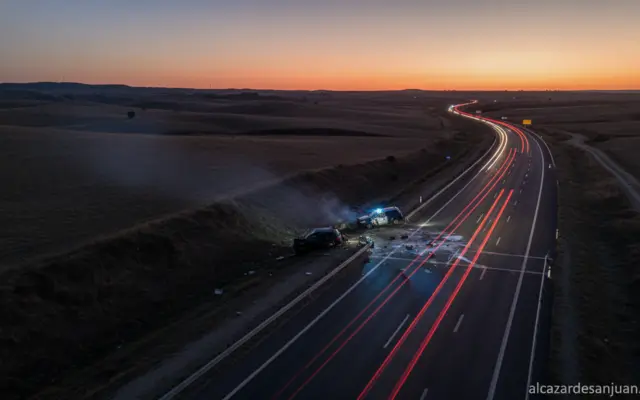A serious scene of a highway in Castilla-La Mancha, Spain, at dusk with police lights in the background near a car collisi...