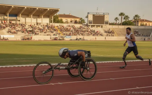 Disabled athlete competing in athletics track, wheelchair racing or adapted running, stadium in Spain, natural daylight, j...