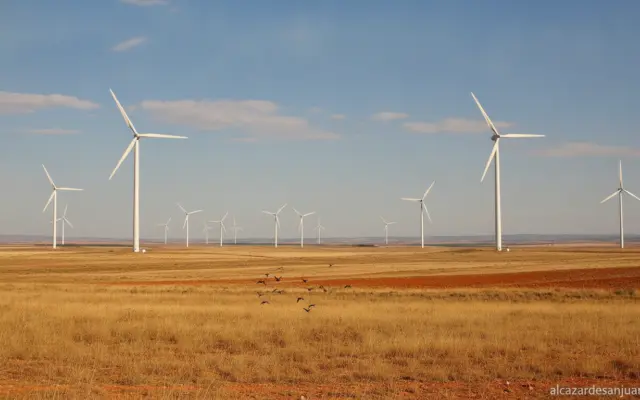 Landscape photograph of wind turbines on a dry steppe plain in Castilla-La Mancha, Spain. A small flock of birds flies in ...