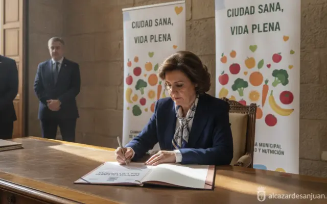 Realistic photojournalism style image of a Spanish mayor signing an official municipal adhesion document at a city hall de...